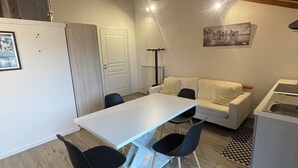 A modern kitchen with a white countertop, black chairs, a white sofa, and a cityscape painting on the wall. - Homely - Malpensa & Fiere Milano (Cardano al Campo)