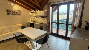 A modern kitchen with a dining area, wooden ceiling beams, and a large window with a view. - Homely - Malpensa & Fiere Milano (Cardano al Campo)