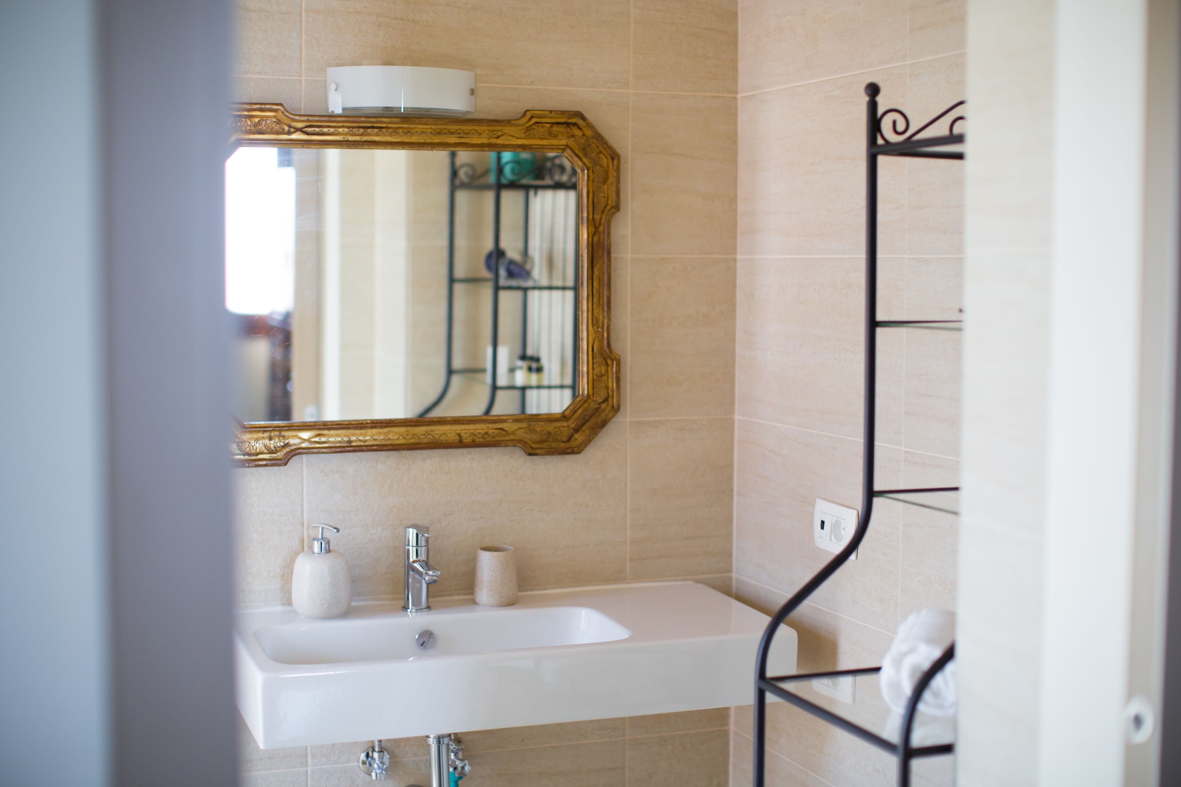 A bathroom with a white sink, a gold-framed mirror, and a black metal towel rack.