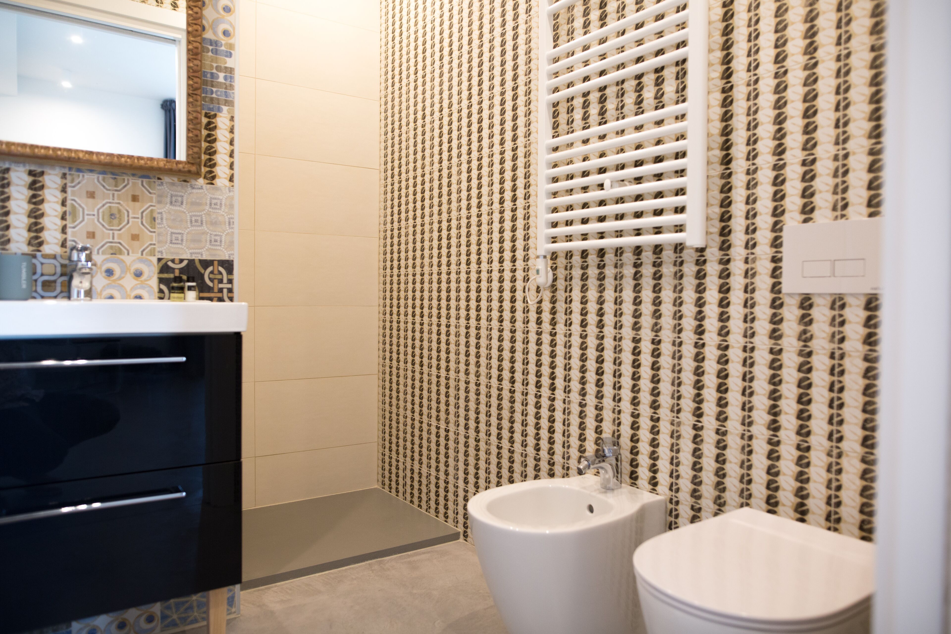 Une salle de bain moderne avec un papier peint à motifs, un meuble-lavabo noir doté de tiroirs, un lavabo blanc et un bidet.