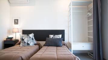 A hotel room with two beds, a bedside table with a lamp, a wardrobe, and a framed picture on the wall.