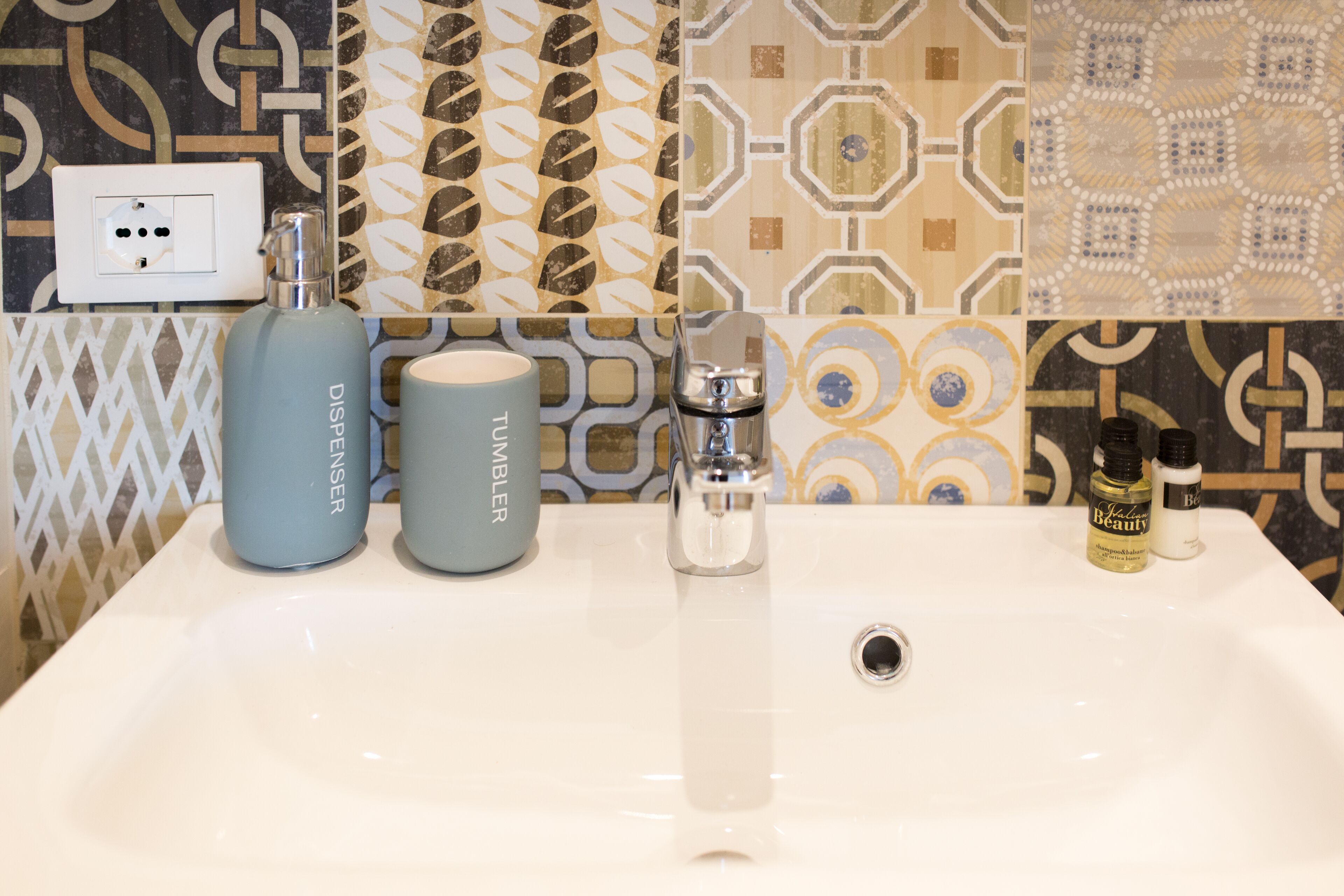 A bathroom sink with two dispensers, a faucet, and patterned tiles.