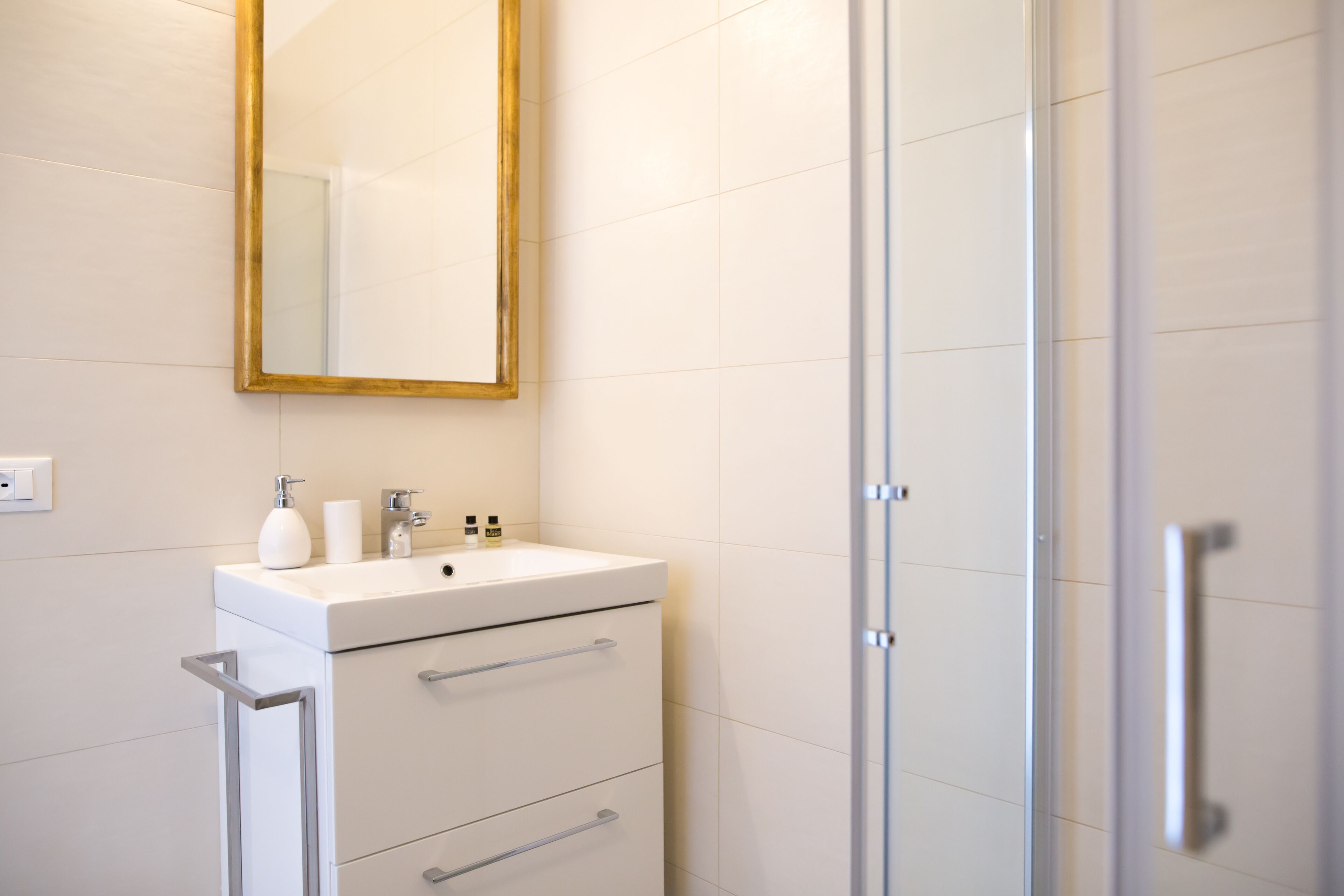 Un baño con un lavamanos blanco, un espejo con marco dorado y una puerta de ducha de vidrio.