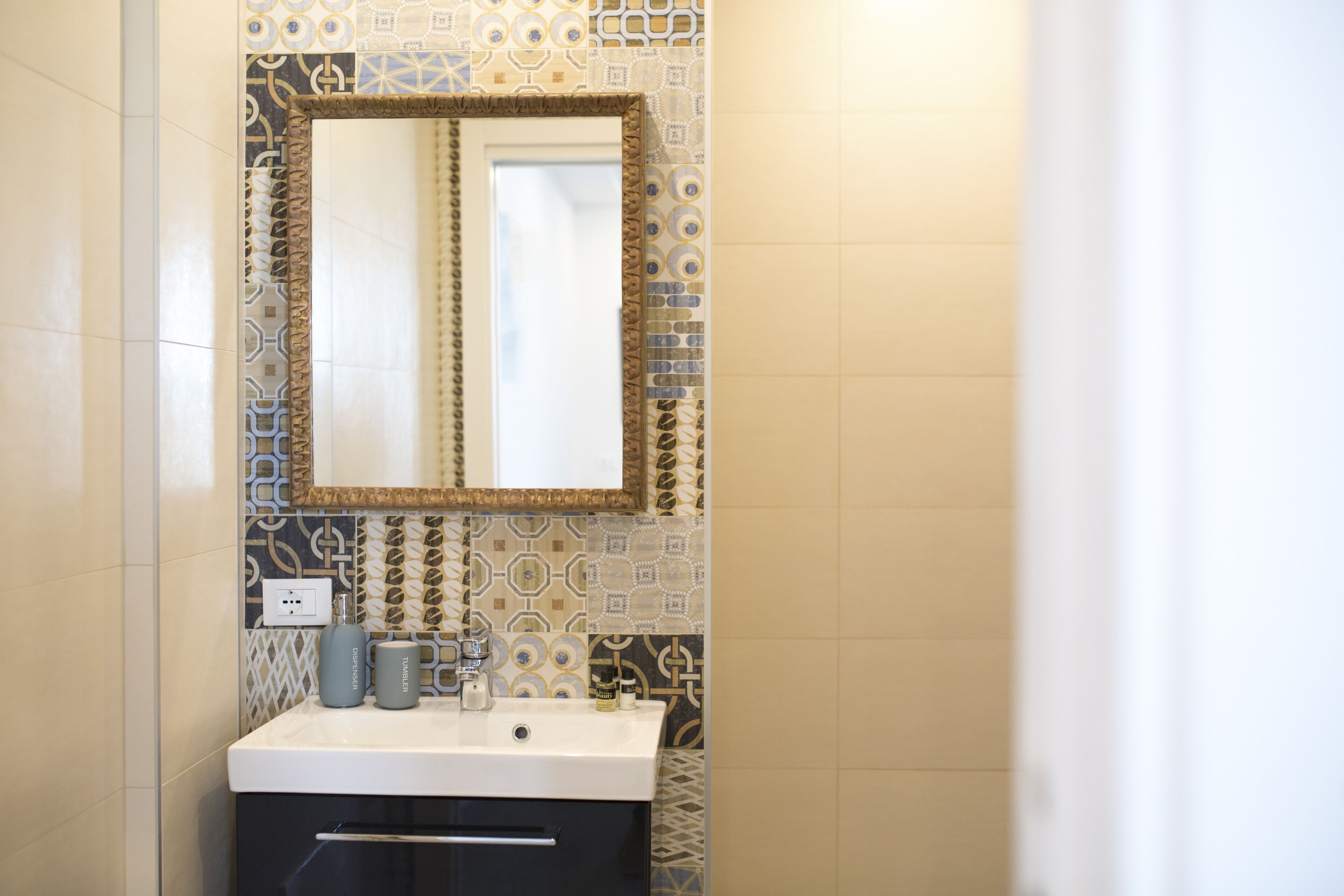 A bathroom with a white sink, a mirror with a decorative frame, and patterned tiles on the walls.