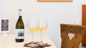 Ett bord med en vinflaska och två glas vitt vin, en inramad tavla på väggen och en trästol.