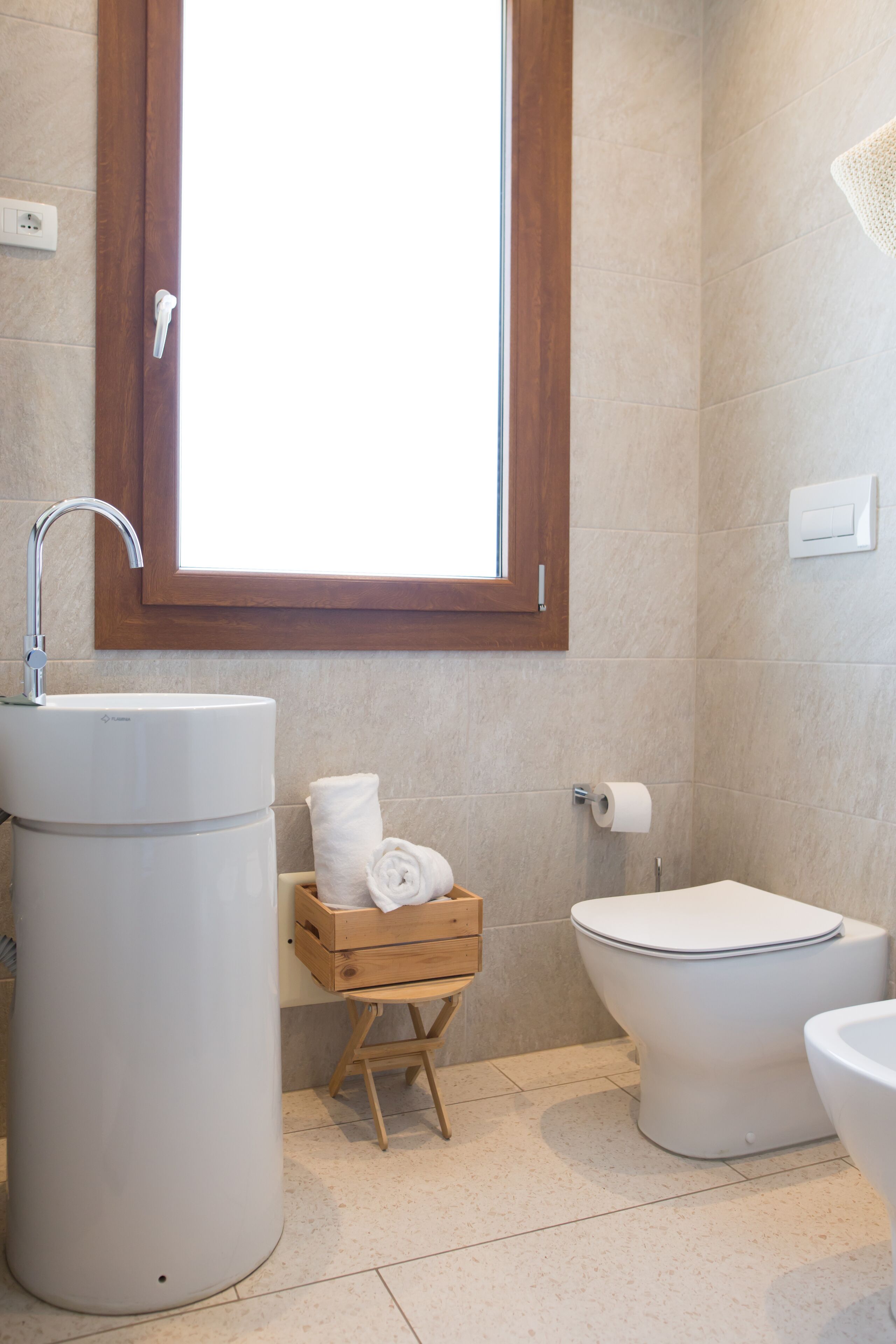 A bathroom with a large sink, toilet, and a wooden bench with towels.