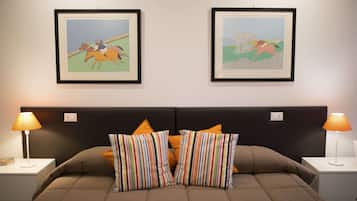 A neatly made bed with striped pillows, two framed horse racing paintings on the wall, and two bedside lamps on either side.
