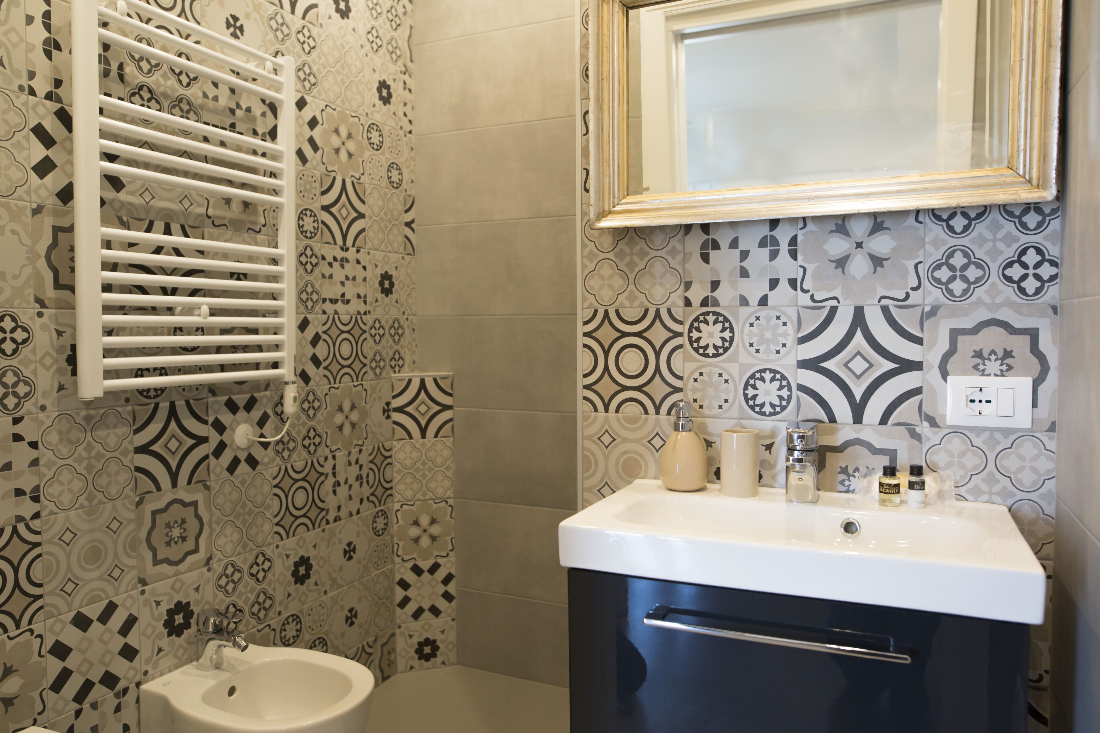 A bathroom with patterned tiles, a white sink, and a mirror above it.