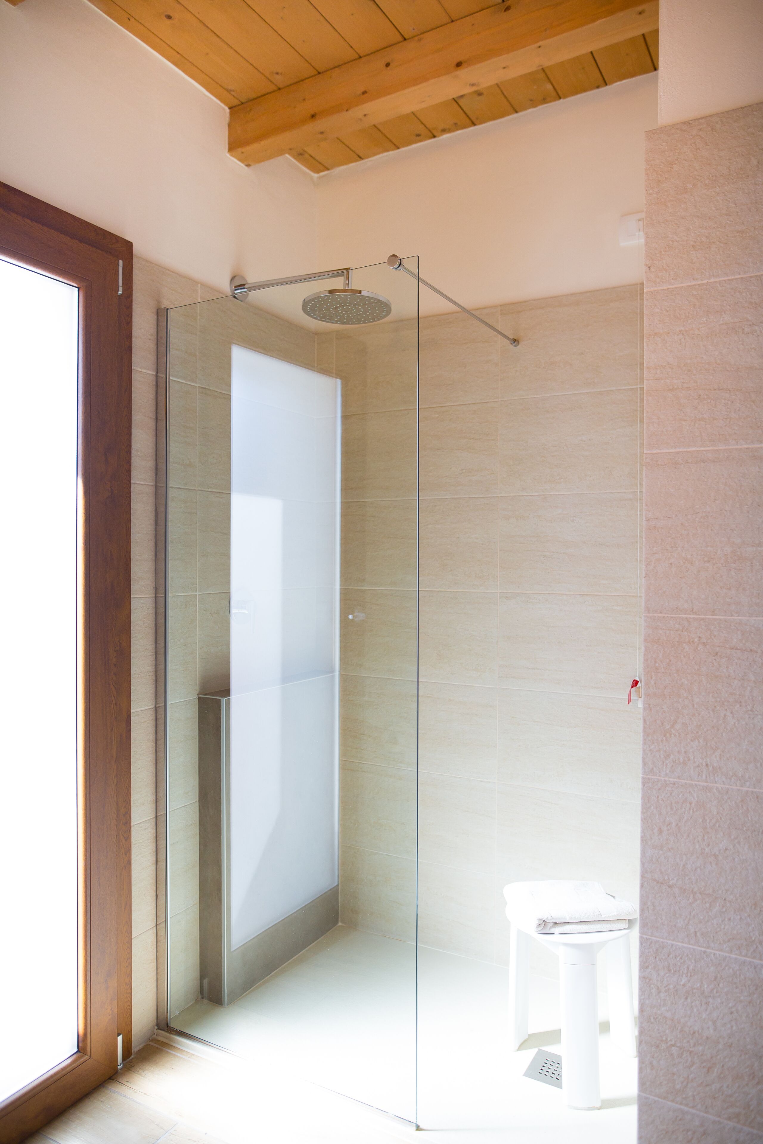 A modern bathroom with a glass shower enclosure, a white toilet, and a wooden ceiling.