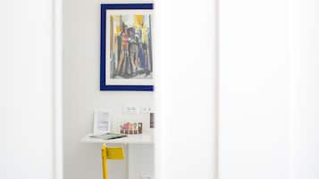 Una habitación con un escritorio blanco, un cuadro abstracto enmarcado y una silla amarilla.