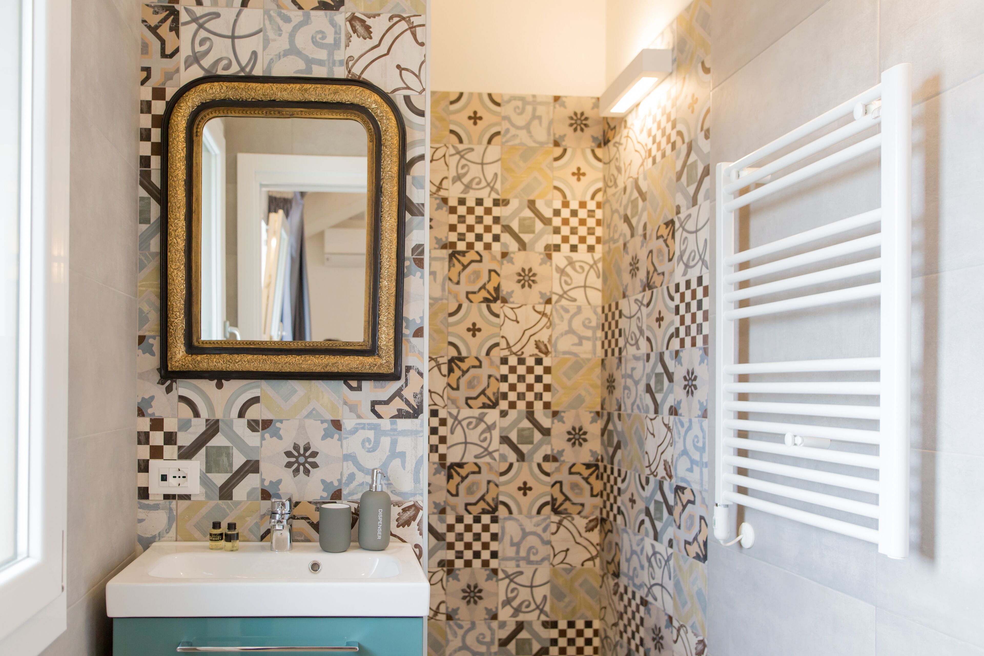 A bathroom with patterned tiles, a sink with a mirror, and a white towel rack.