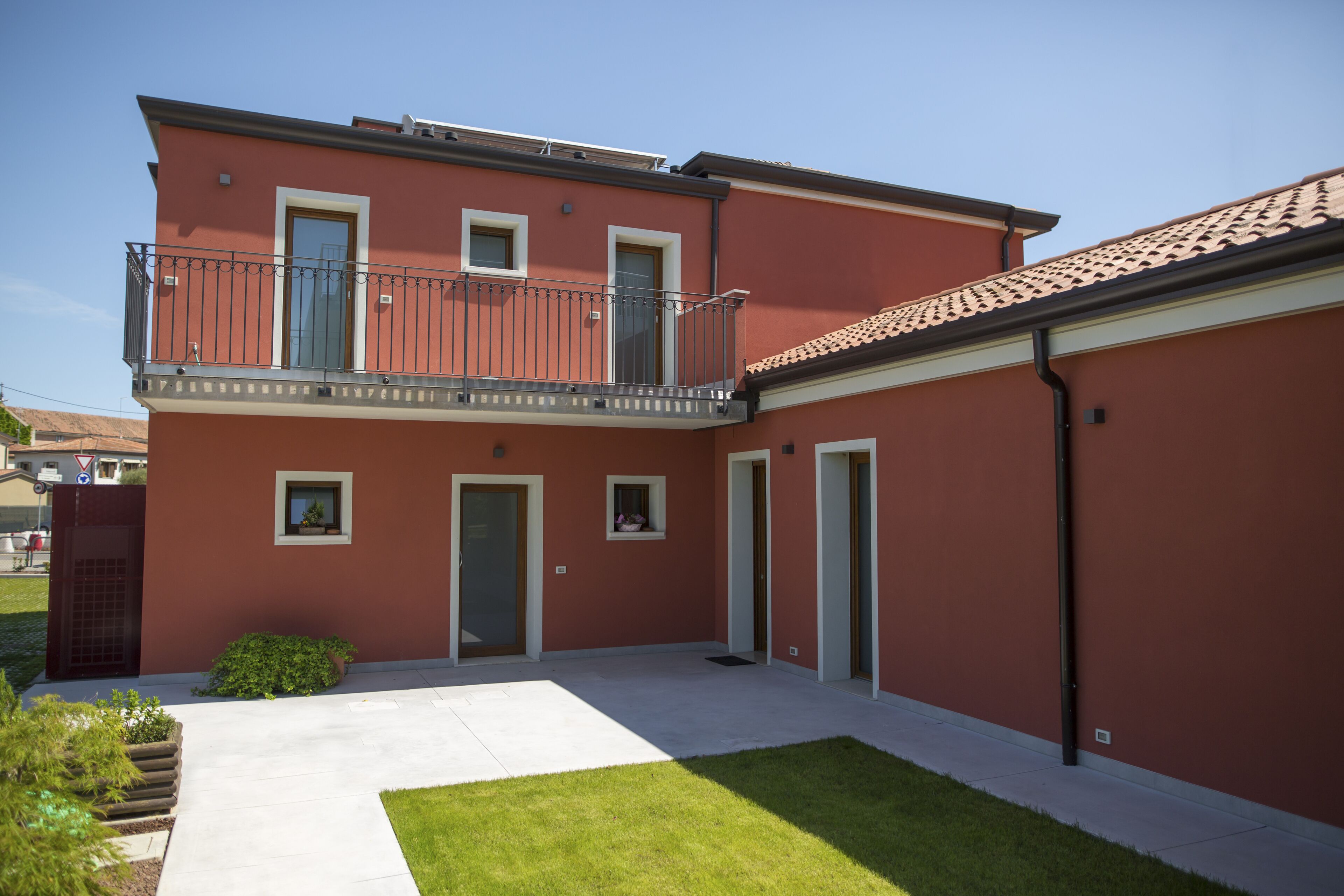 A two-story building with a balcony, a small garden, and a paved driveway.