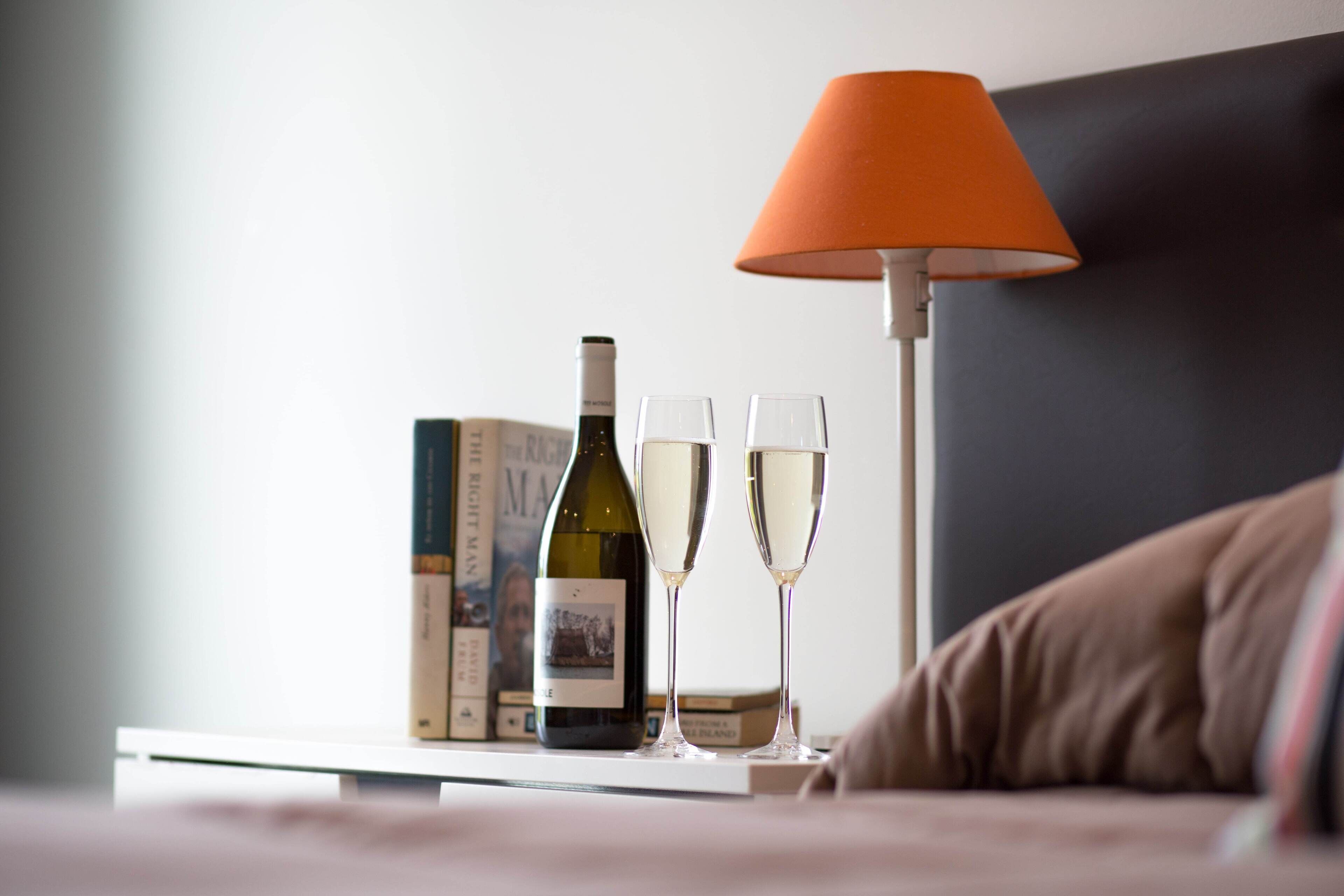 A bedside table with a wine bottle, two glasses, and a book.