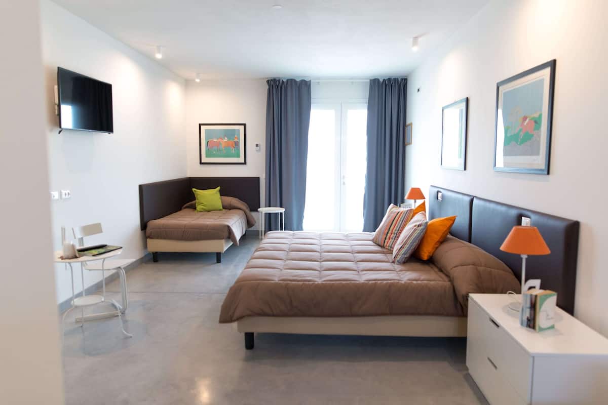 A modern bedroom with a large bed, a smaller bed, a desk, and a TV.