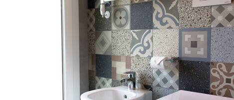 Un bagno con un lavandino bianco, un WC e una parete rivestita di piastrelle decorate.