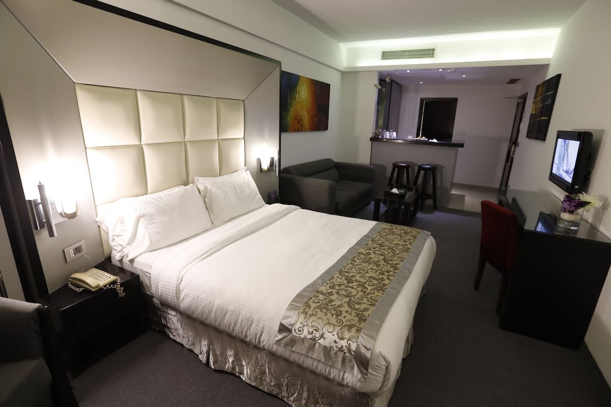 Une chambre d’hôtel avec un grand lit, un bureau, une chaise, une télévision et un petit coin cuisine.