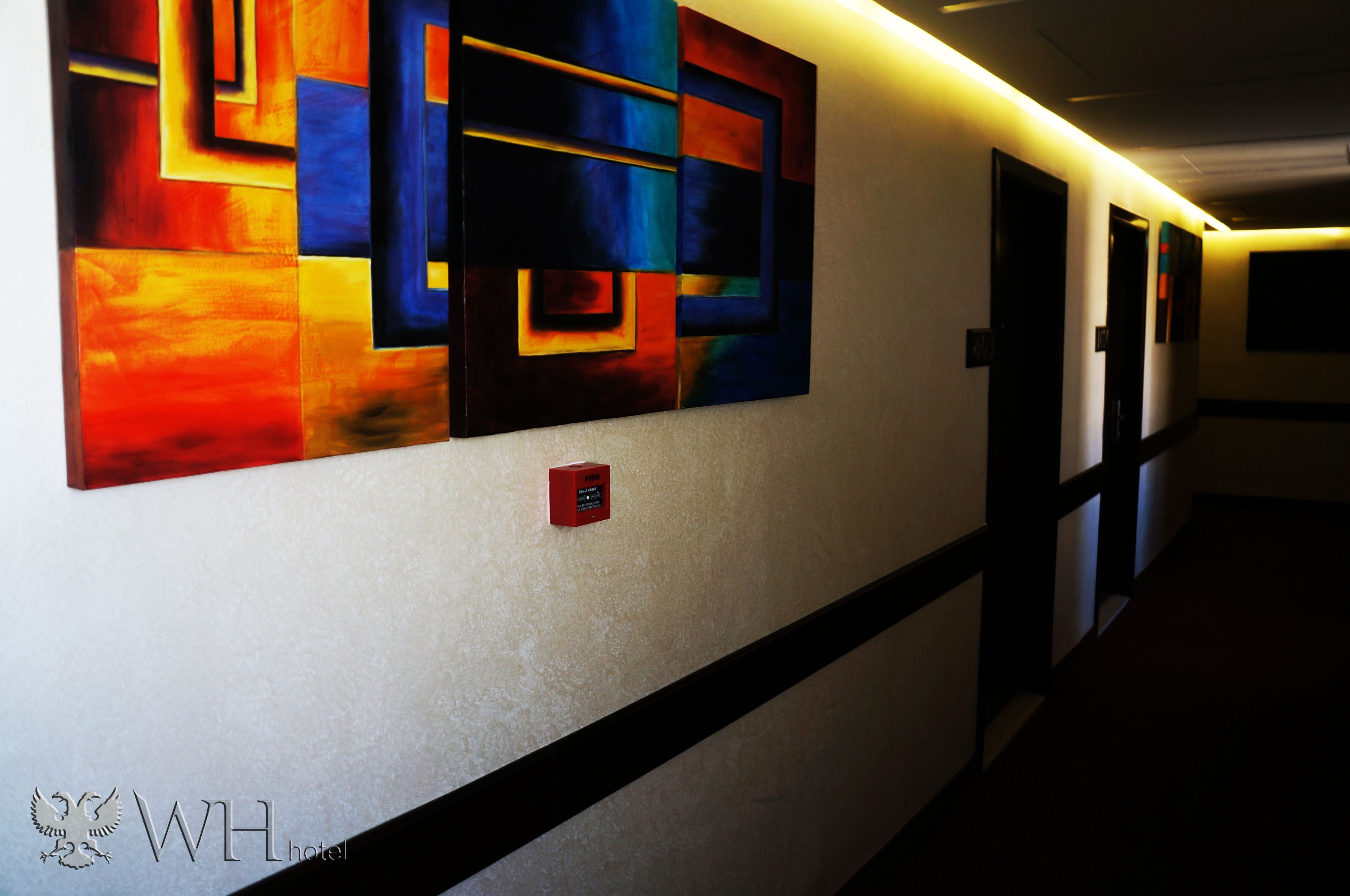 Corredor com arte abstrata na parede, um alarme de incêndio e uma faixa preta ao longo do chão.
