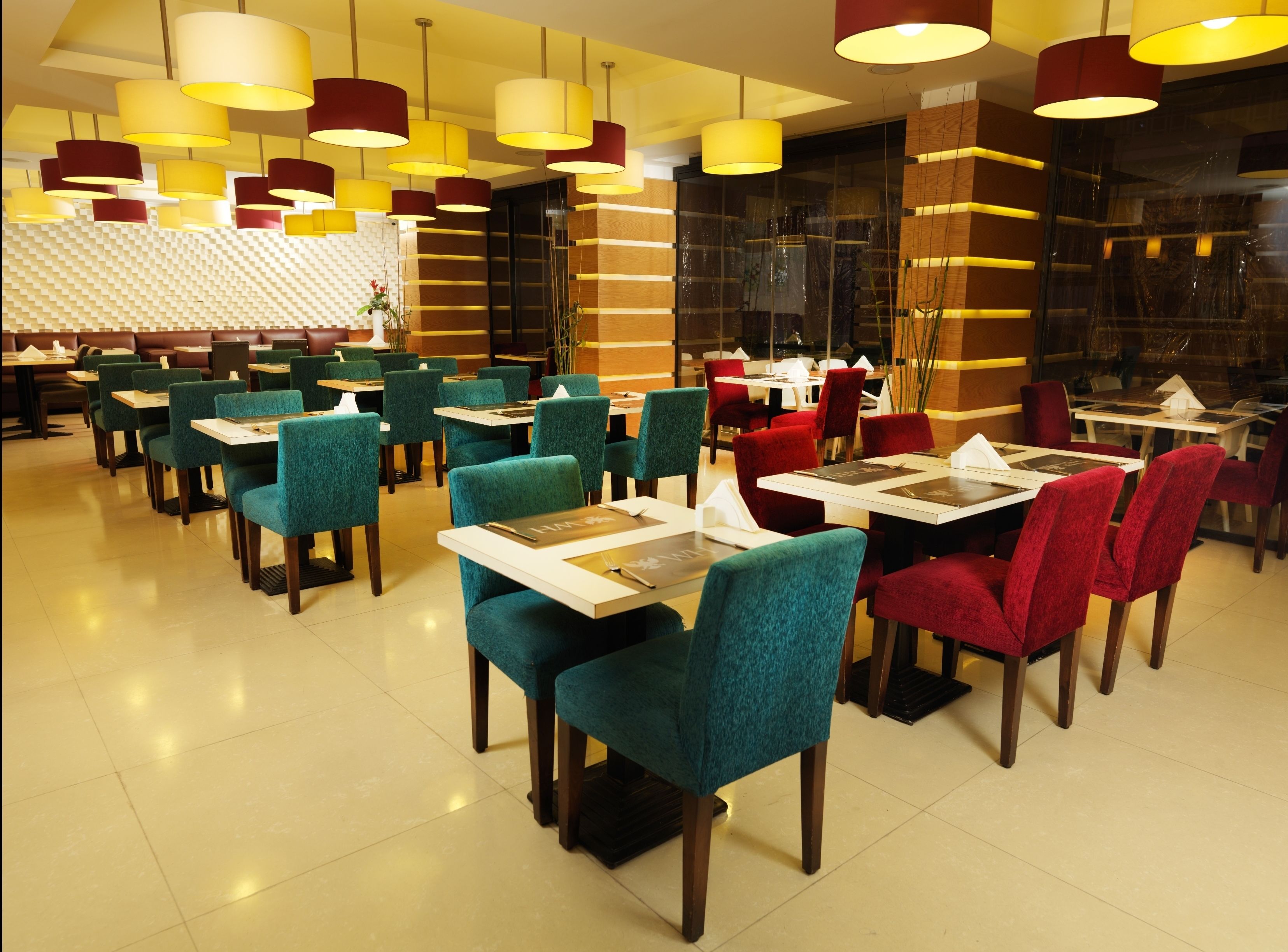 A restaurant with teal and red chairs, white tables, and yellow and red pendant lights.