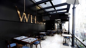 A modern hotel interior with a large 'WH' sign, multiple tables and chairs, and a view through a glass wall. - WH Hotel (Beirut)