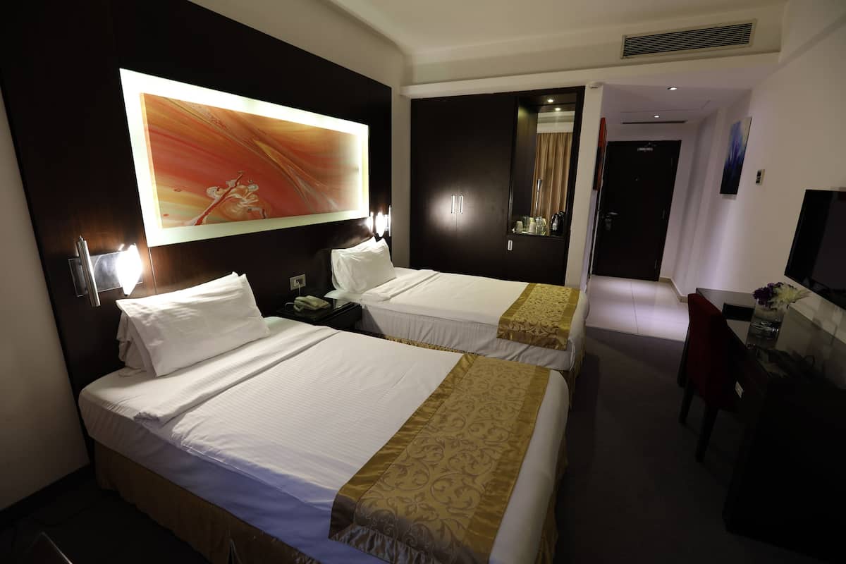 Une chambre d’hôtel avec deux lits, un bureau, une chaise, une télévision et un grand tableau au mur.