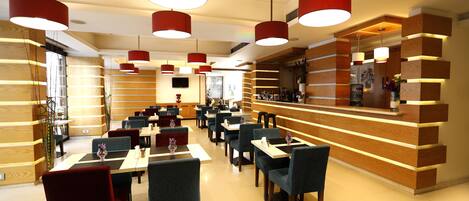 Ein modernes Restaurant mit Holzverkleidung, roten Pendelleuchten und ordentlich angerichteten Tischen und Stühlen.