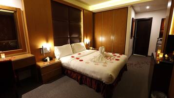A hotel room with a large bed, a bedside table, a desk, and a mirror.