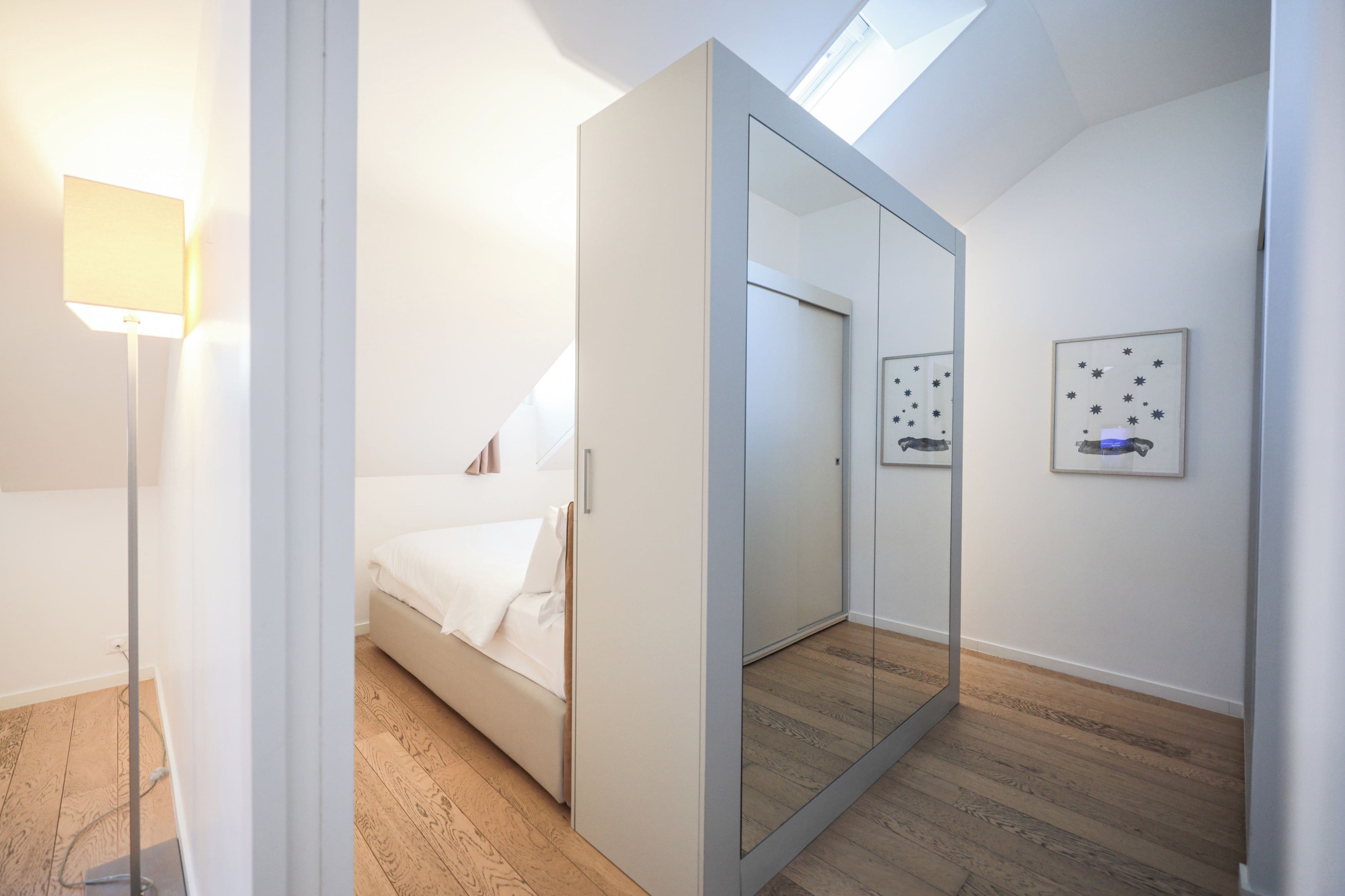 Un dormitorio moderno con una cama, un espejo grande, un armario y un tragaluz en el techo.