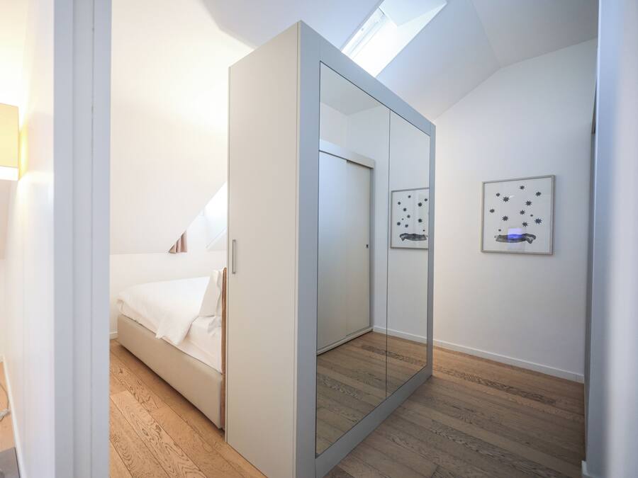 Un dormitorio moderno con una cama, un espejo grande, un armario y un tragaluz en el techo.
