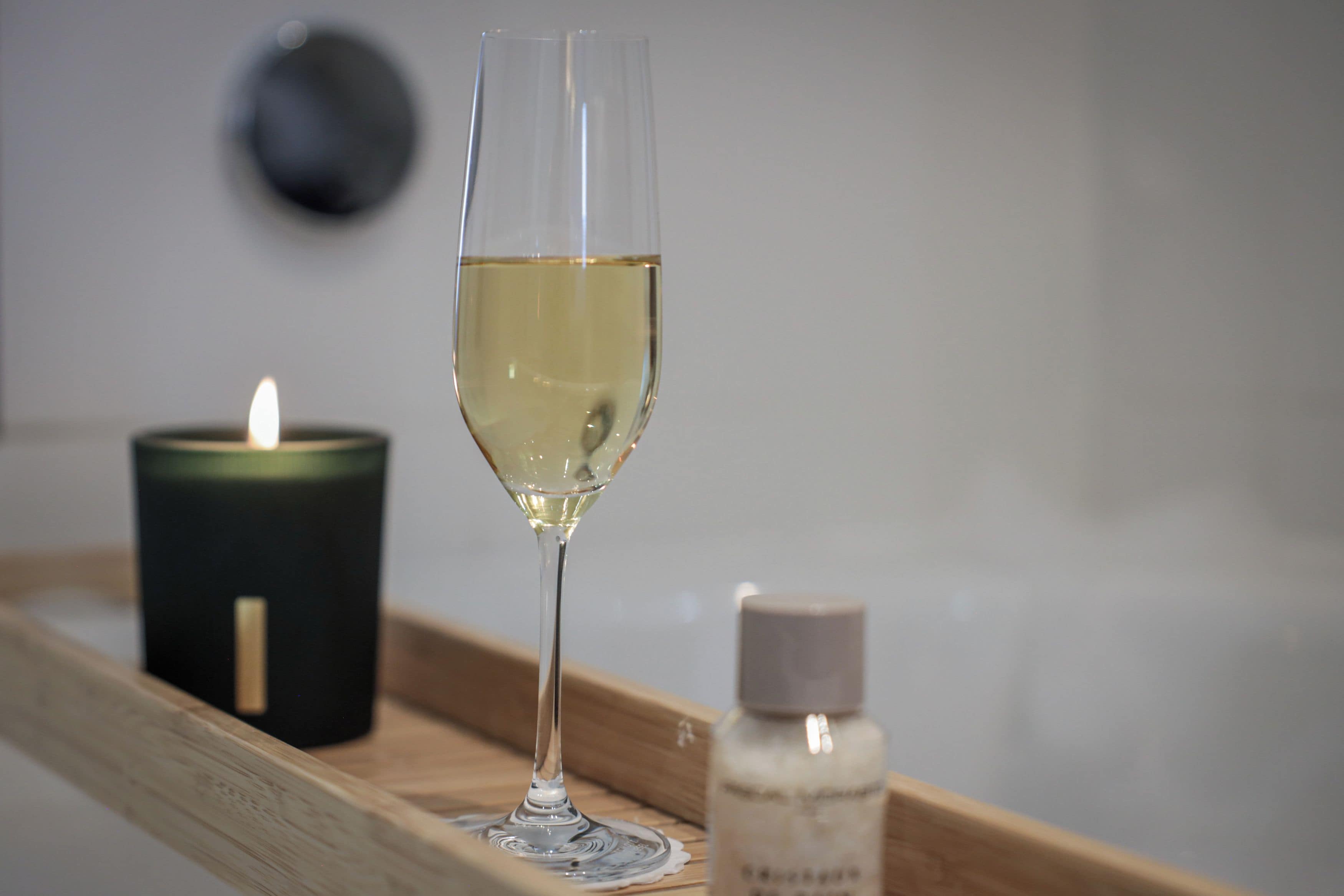 Una copa de vino blanco sobre una bandeja con una vela encendida y una botella de perfume.