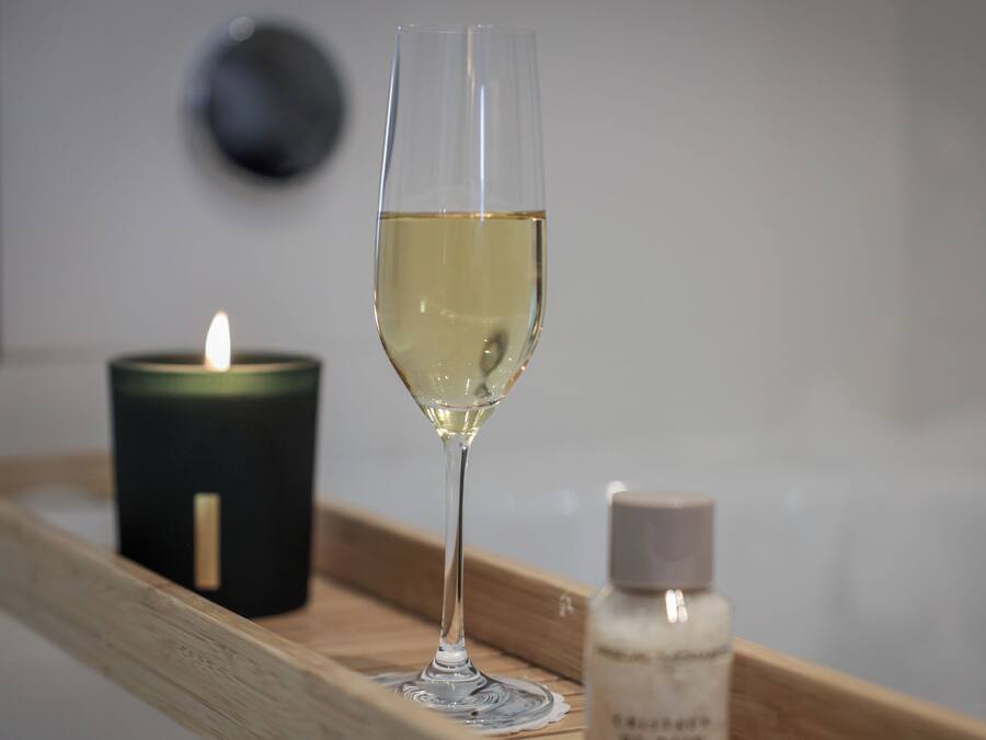 Una copa de vino blanco sobre una bandeja con una vela encendida y una botella de perfume.