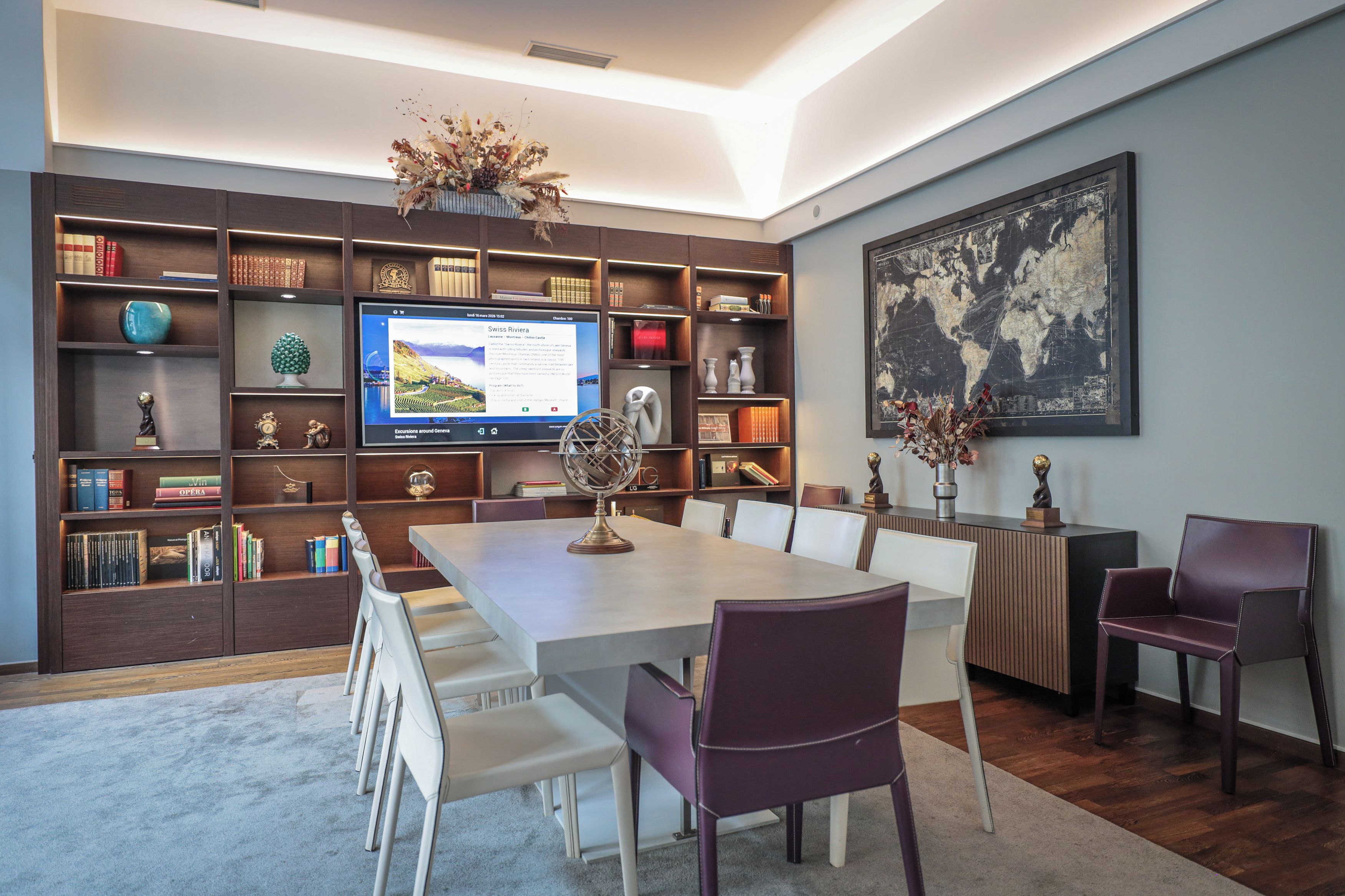 A modern dining area with a long table, white chairs, and a bookshelf filled with books and decorative items.