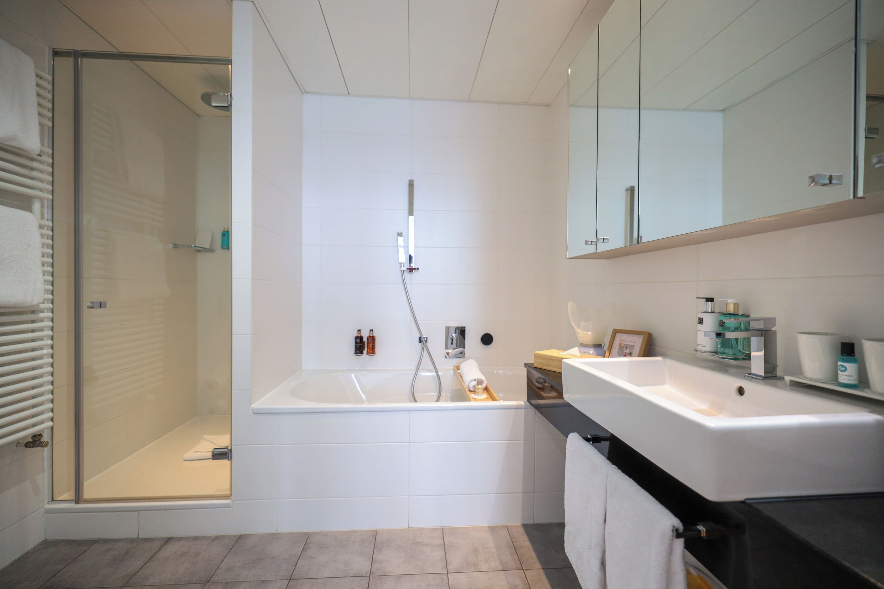 Un baño moderno con cabina de ducha de vidrio, una bañera y un lavamanos con espejo.