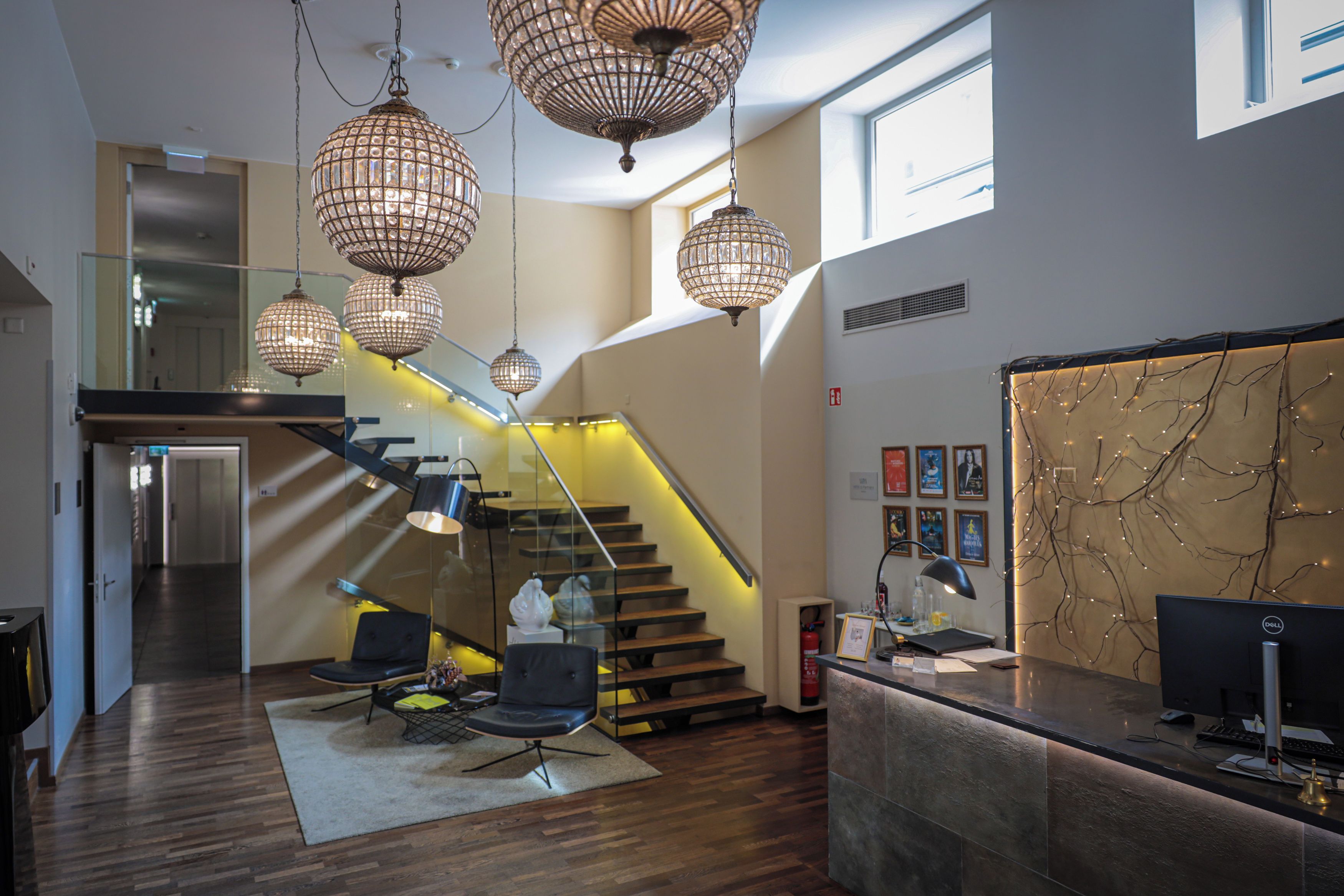 A modern interior with a reception desk, a staircase with glass railings, and decorative lighting fixtures.