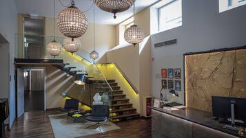 A modern interior with a reception desk, a staircase with glass railings, and decorative lighting fixtures.