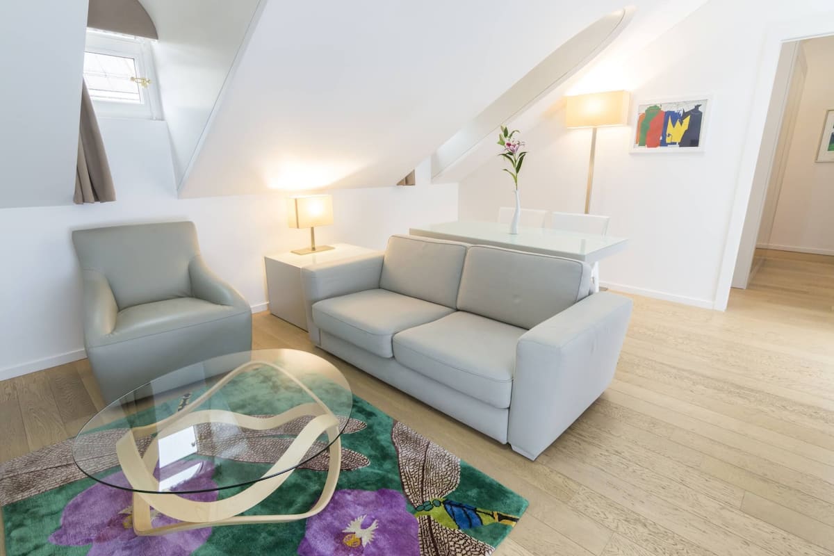 A modern living room with a glass coffee table, grey sofas, and a wooden floor.