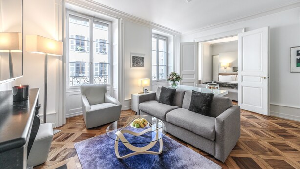 A modern living room with a sofa, armchairs, a glass coffee table, and a dining area with a table and chairs. - Swiss Luxury Apartments Geneva (Geneva)