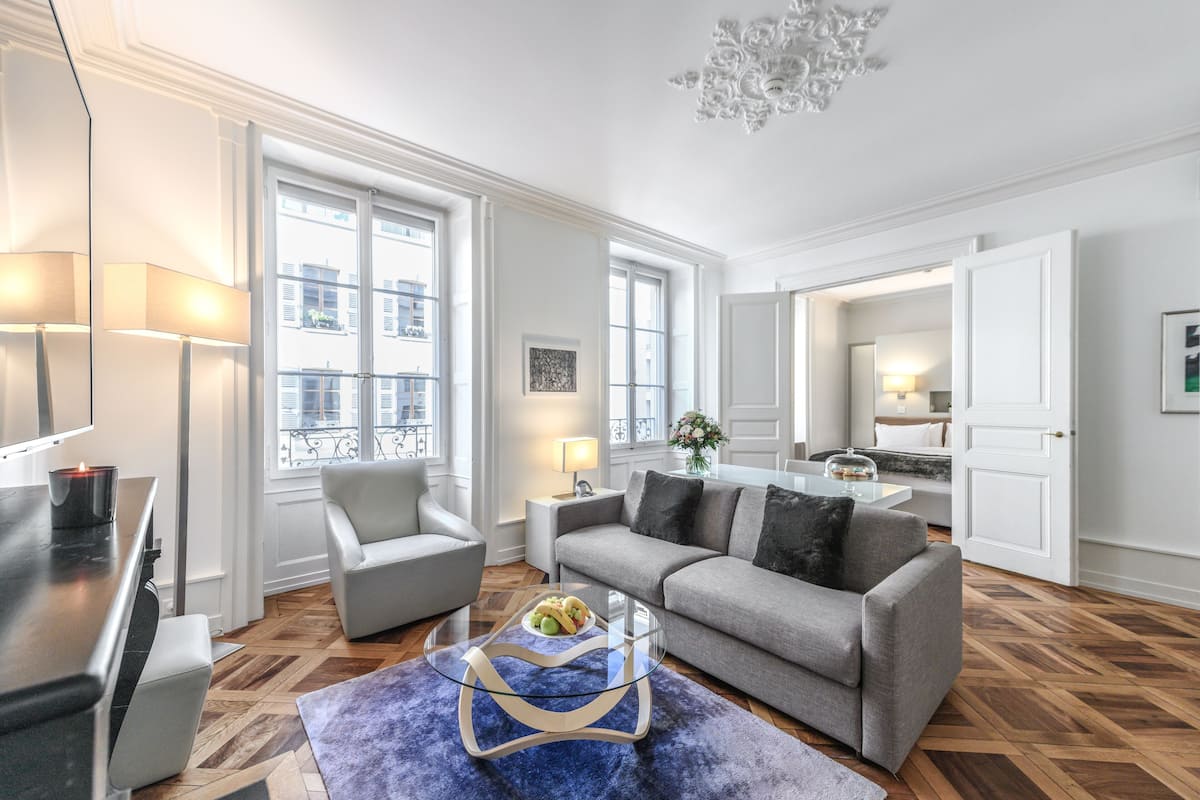 A modern living room with a sofa, armchairs, a glass coffee table, and a dining area with a table and chairs.