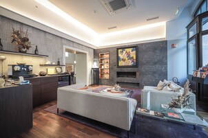 Una sala de estar moderna con sofá, mesa de centro y chimenea. Cuenta con una zona de cocina con cafetera y mesa de comedor.