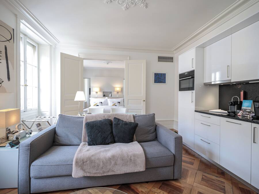 Een moderne woonkamer met een grijze bank, een koffieapparaat en een keuken met witte kasten.
