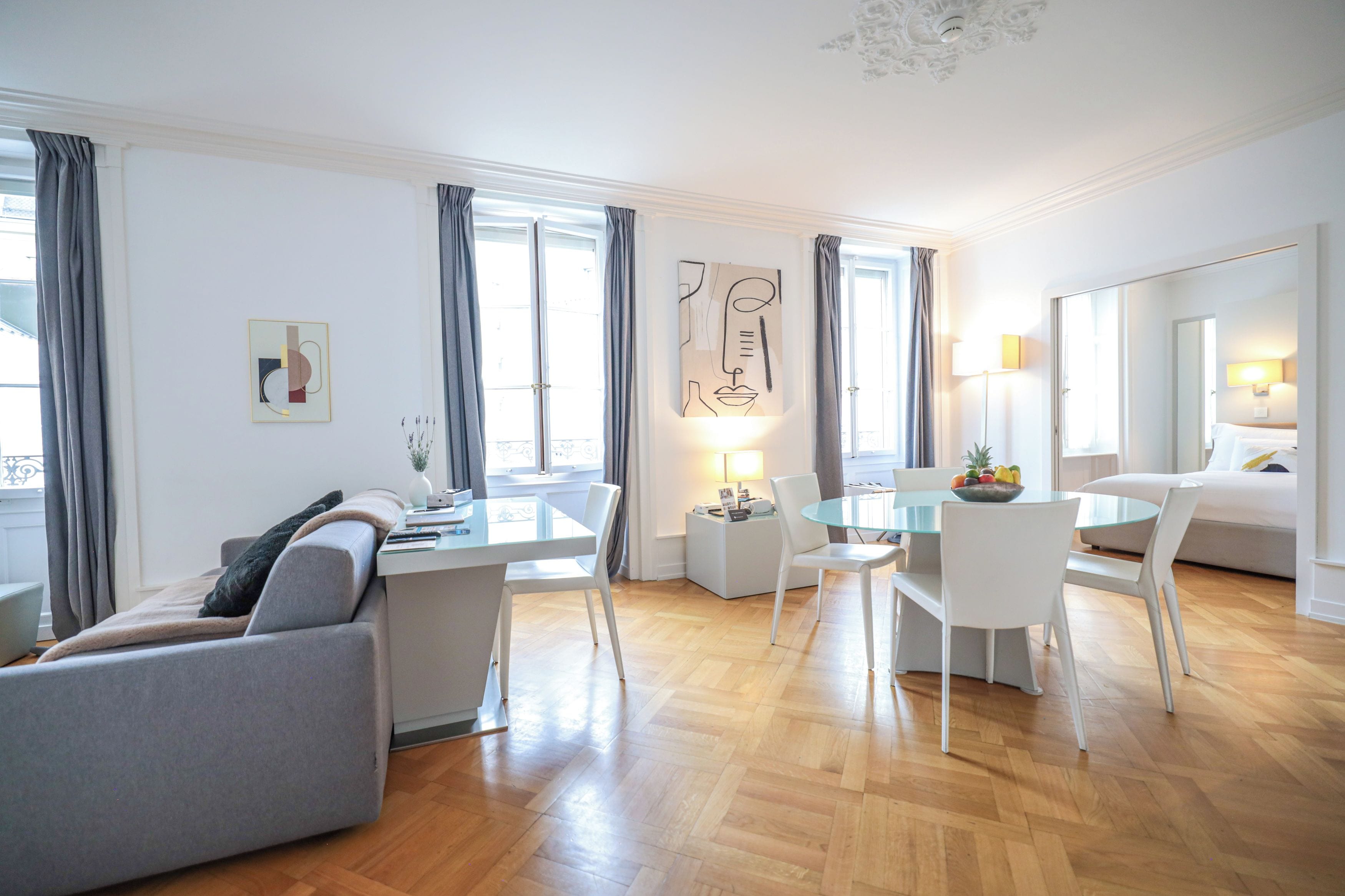 Una sala de estar moderna con un sofá, una mesa de comedor de vidrio y una zona de cocina con un refrigerador y una lámpara.