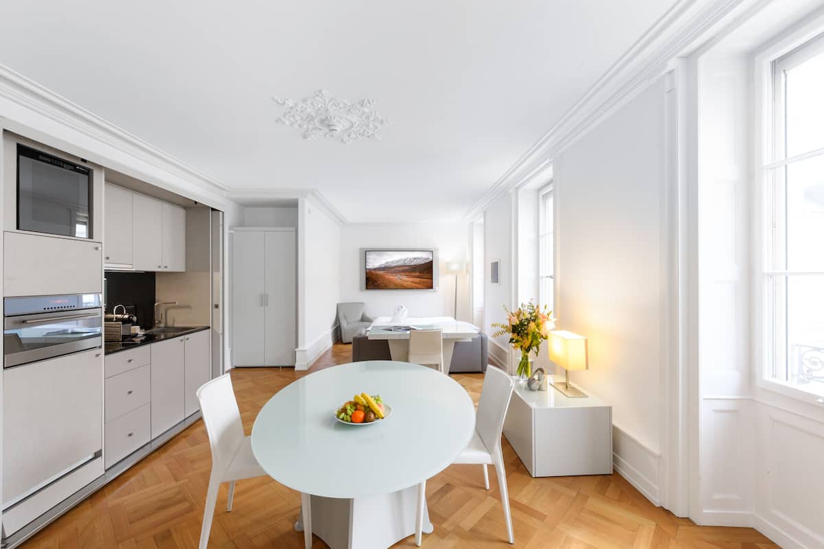 A modern kitchen with white cabinets, a dining table with chairs, and a fruit bowl.