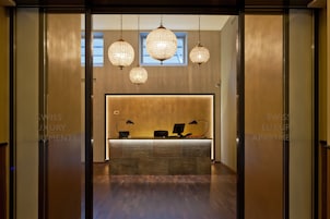 A reception area with a modern design, featuring a reception desk, three pendant lights, and a view of the outside through a window.