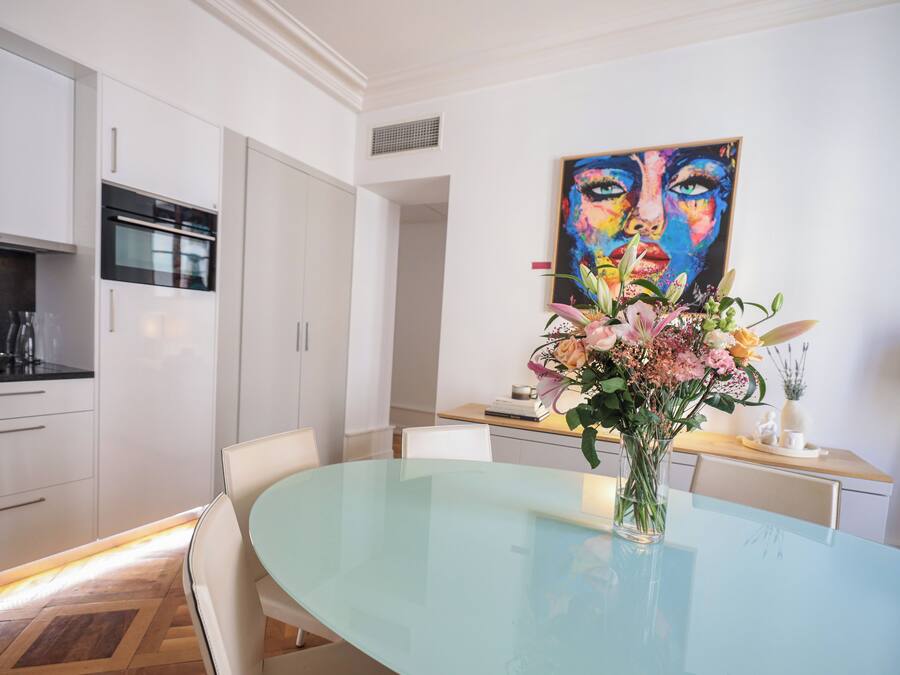 A modern kitchen with white cabinets, a built-in oven, and a dining area with a glass table and chairs.