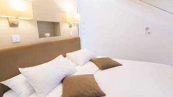 Una cama bien hecha con almohadas blancas y marrones, un cabecero y dos lámparas fijadas a la pared.