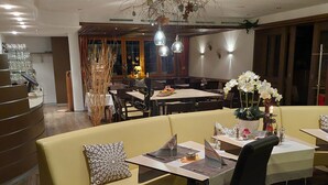 A modern restaurant with a mix of seating options including a bar area, a dining area with tables and chairs, and a lounge with sofas. - Hotel GARNI Mittenwald (Flums)