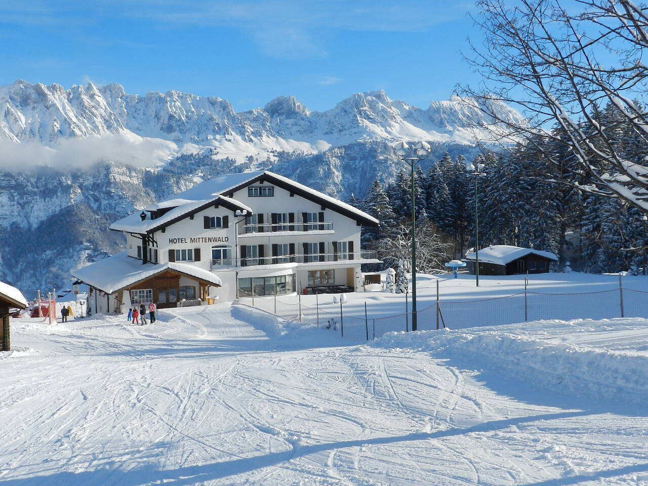 A hotel with a modern design, a ski slope in the foreground, and snow-covered mountains in the background.
