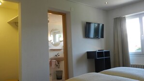 A hotel room with a bed, a TV mounted on the wall, a small sink, and a window with curtains. - Hotel GARNI Mittenwald (Flums)