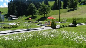 A landscaped garden with seating areas, a pathway, and a small building in the background. - Hotel GARNI Mittenwald (Flums)