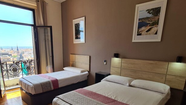 Un cuarto de hotel con dos camas, un balcón con vista a la ciudad y un cuadro en la pared.