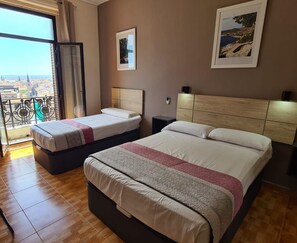 A hotel room with two beds, a balcony with a view of the city, and a framed picture on the wall.